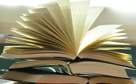 Kilka otwartych książek leżących jedna na drugiej.