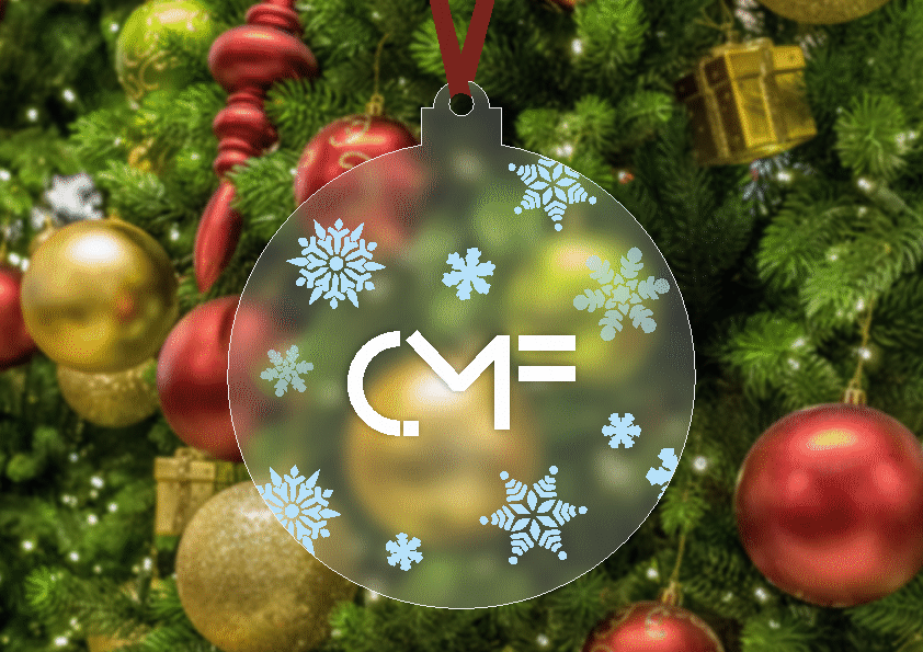 Bombka choinkowa z logo CMF, ozdobiona motywami śnieżynek, zawieszona na choince z czerwonymi i złotymi ozdobami w tle.